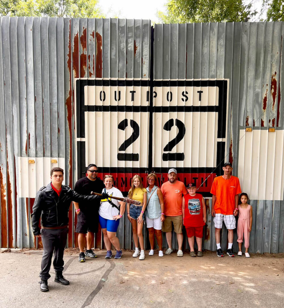 A group of people standing in front of a the iconic Outpost 22 sign from the Walking Dead