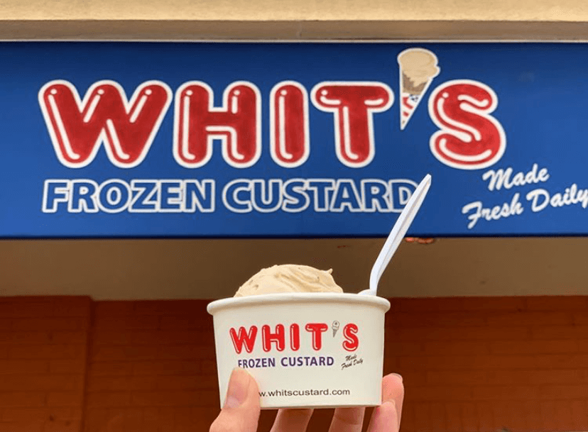 Scoop of Whit's frozen yogurt in a cup in front of the store logo
