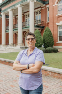 Woman standing in front of columns in purple shirt with glasses