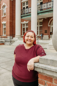 Woman in red sweater standing in front of column with arm propped up