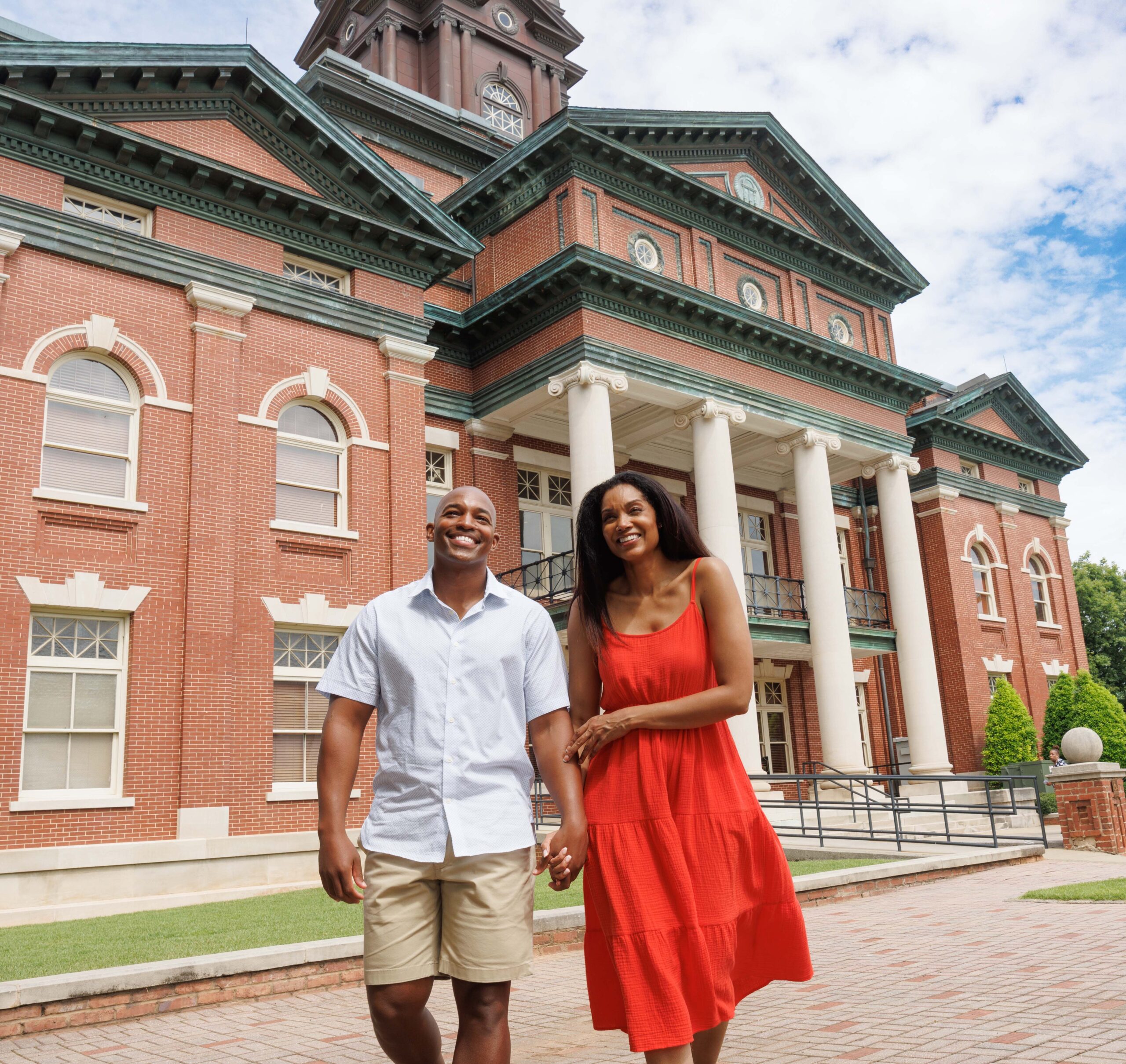 Couple holding hands in front of historic courthouse and smiling