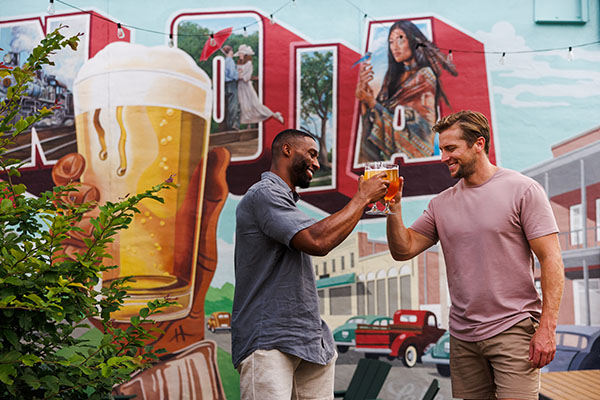 2 guys holding beers infront of mural