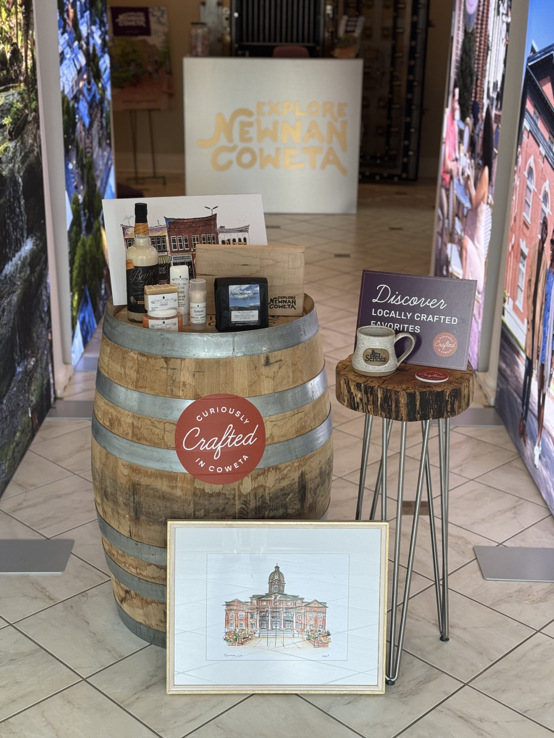 Brand shot including a barrel, 2 art pieces, skin care products, coffee beans and a coffee mug, bourbon cream, and wood work.