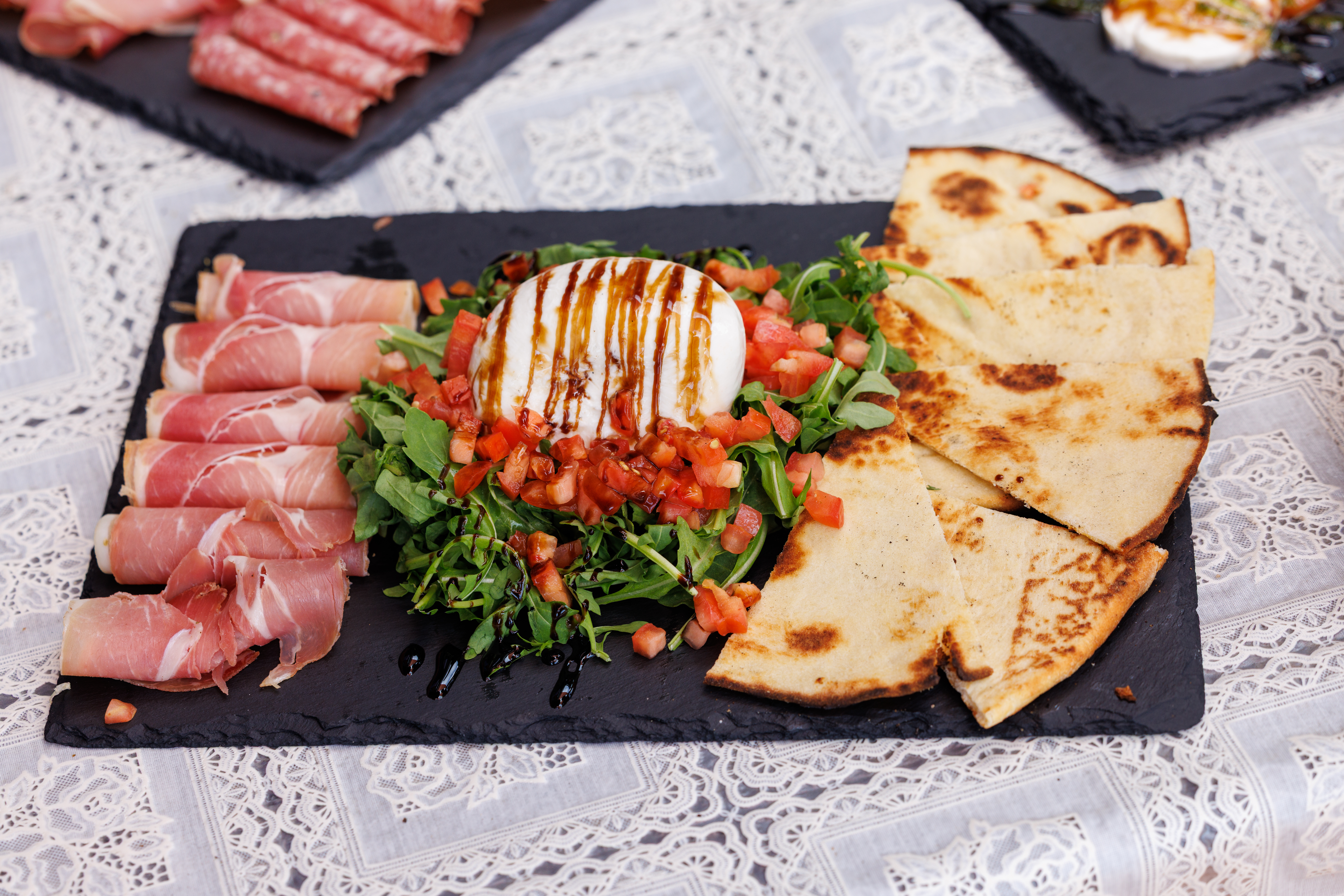 slate board with prosciutto, burrata and pita bread slices
