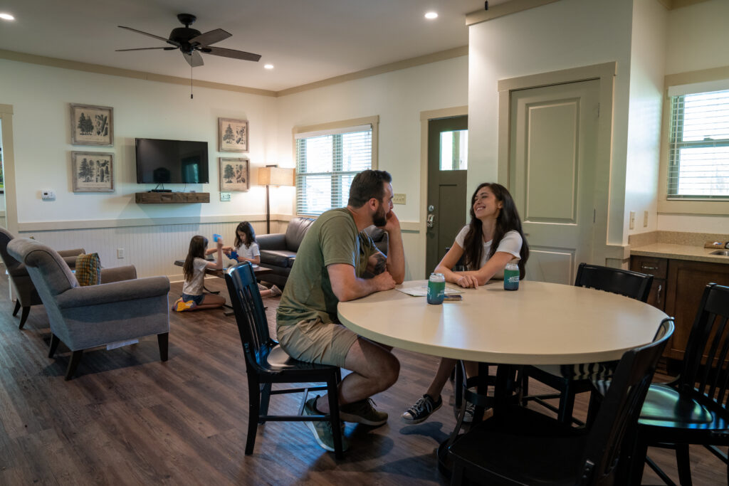 Family relaxing inside cabin with couple sitting at table and children playing on floor