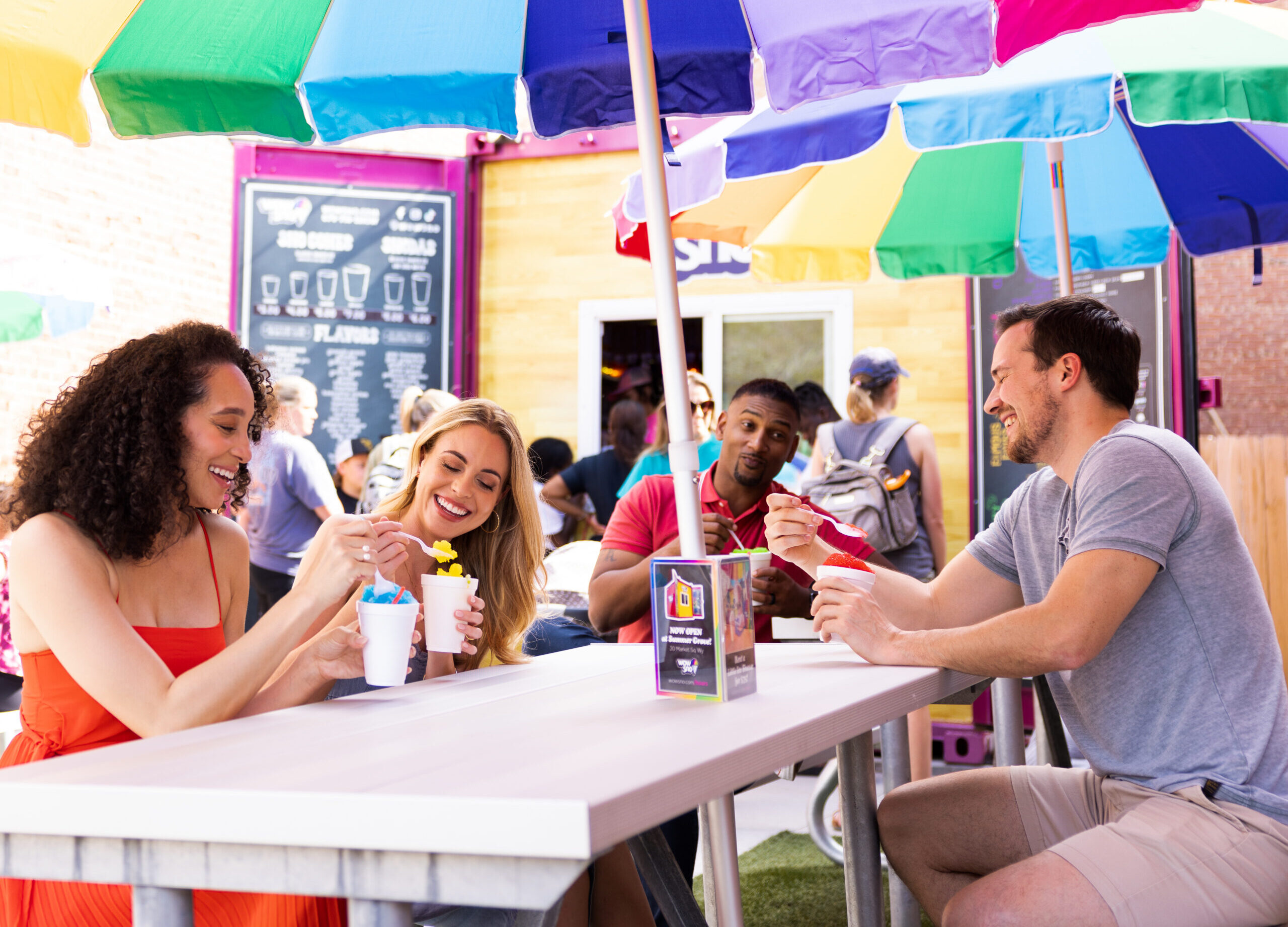 Group of friends eating snoballs outside under a rainbow umbrella